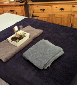 Massage couch in licing room with dark blue fleece and light blue sheet. Oils and towels are on the couch ready for a client.